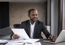 Man in smart jacket sat at a desk working on a laptop