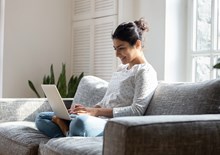 smiling women sat on the sofa working on her laptop