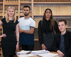 Group of 4 students in front of bookshelf 