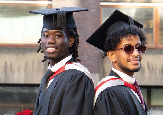 Two students standing back to back wearing graduation dress