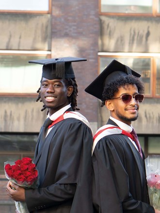 Two students standing back to back wearing graduation dress