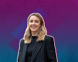 Eleni is a petite white woman with mid-length blonde hair and blue eyes. She is wearing a black top with black pinstripe jacket.